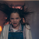 A little girl wearing overalls makes an angry face while her hair stands on end.